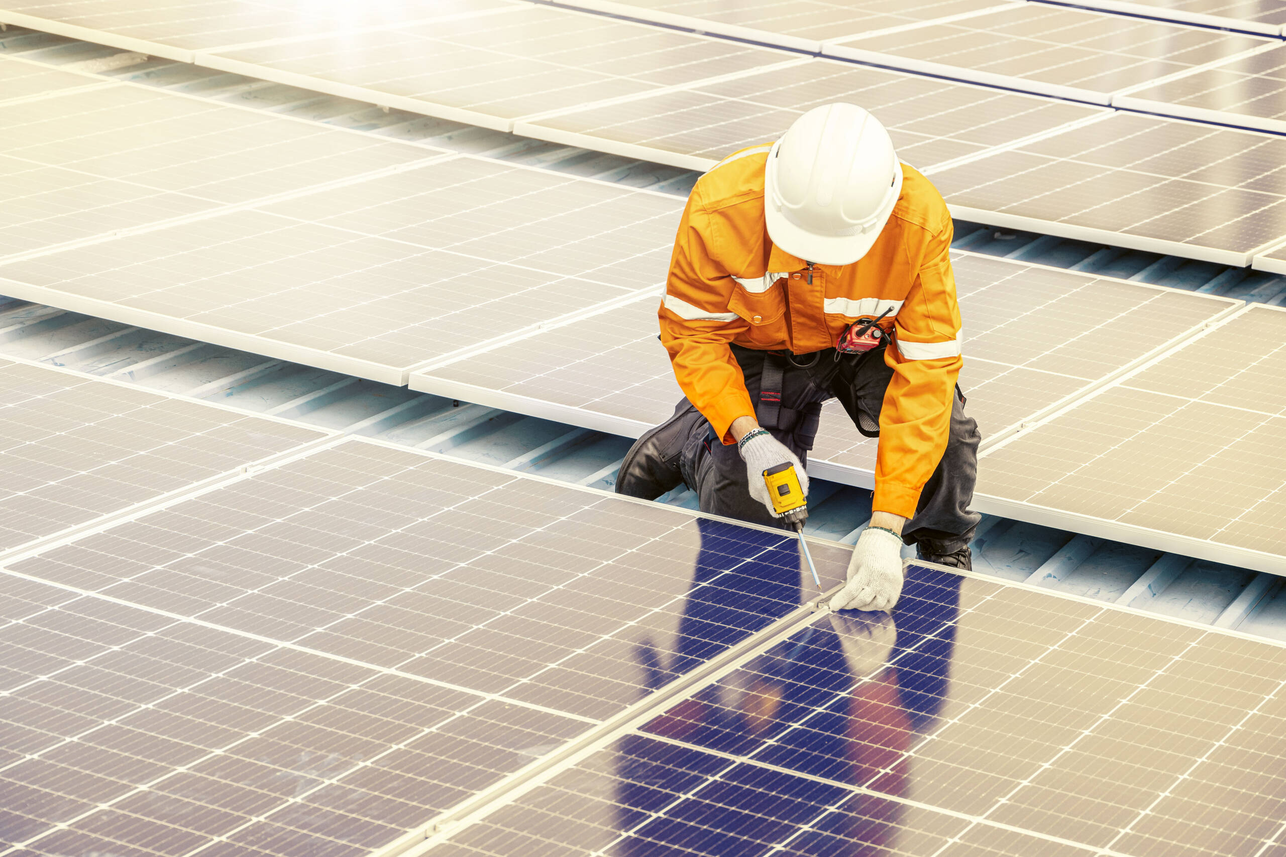 Mann in Arbeitskleidung mit Helm arbeitet an Solarpaneelen
