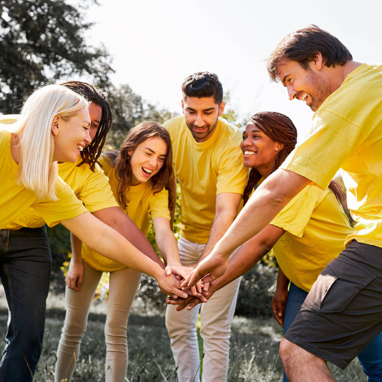 4 Frauen und 2 Männer stehen im Kreis und legen die Hände in ihrer Mitte aufeinander